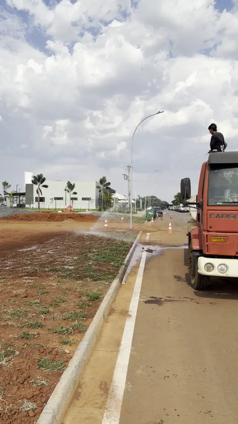 Operador sobre o tanque do caminhão Pipa molhando a área com mangueira